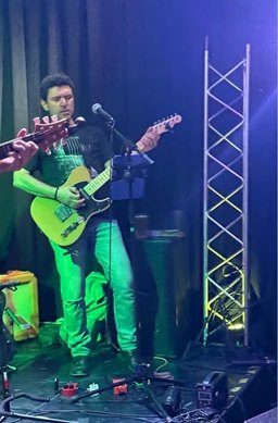 Yener Yardim playing an electric guitar on stage under green light.
